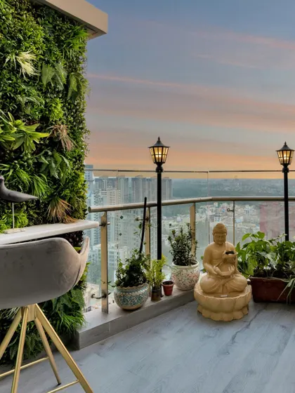 This balcony is a green paradise with a vertical garden wall. A high-top table and chair provide a perfect spot for morning coffee, while a Buddha statue adds a sense of tranquility against the city skyline.