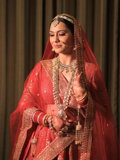 This bride looks serene and beautiful. Her makeup is soft and timeless, designed to complement her intricate jewelry and red lehenga without overpowering her features.