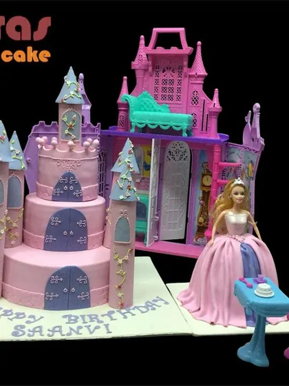 A magical castle cake for Princess Saanvi. This grand setup includes a multi-tiered castle cake alongside a Barbie doll and her playset, creating an entire fairy tale scene.