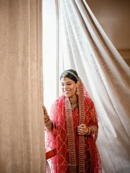 The bride looks out the window with a gentle smile, a quiet moment of anticipation before her Nikah ceremony.