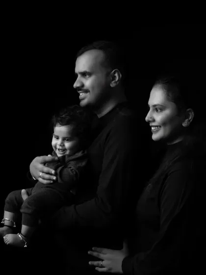 A classic black and white family portrait with parents and their smiling baby against a simple dark backdrop.