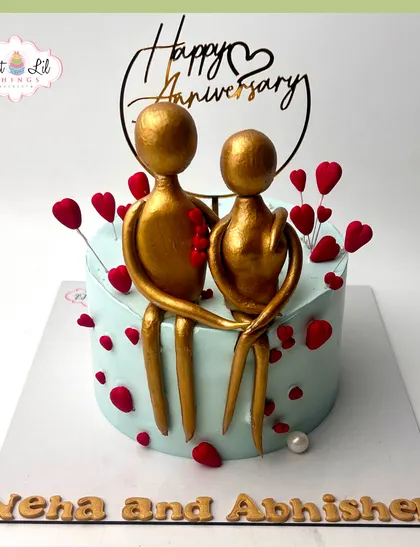 A modern and artistic anniversary cake. This design features abstract golden figures of a couple, surrounded by floating red hearts.
