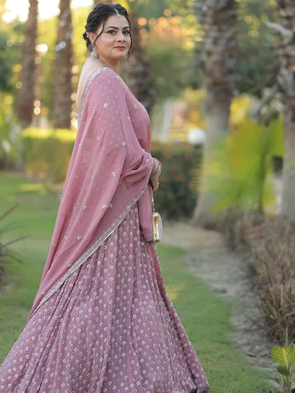 An elegant party guest in a dusty pink lehenga, posing in a beautiful garden setting.