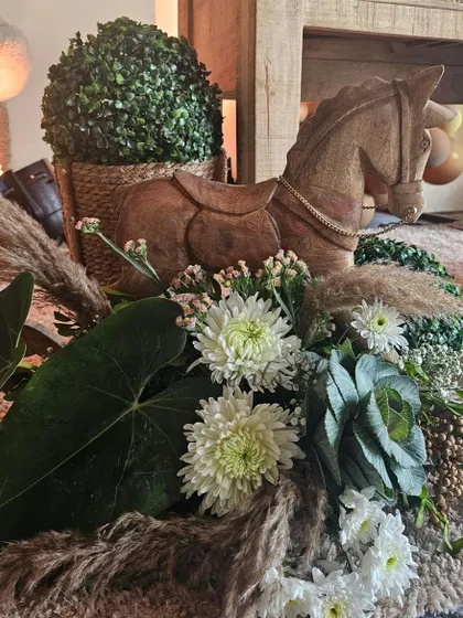 A close-up of a centerpiece from a teddy bear-themed baby shower. A wooden rocking horse and a beautiful floral arrangement with pampas grass create a rustic and charming look.