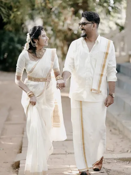 A walking shot of the couple holding hands, dressed in elegant white and gold traditional wear, perfect for a save-the-date or wedding album.