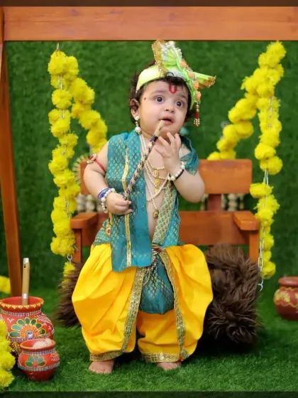 A full-length portrait of a baby in an elaborate Krishna costume, showing the complete look from the crown to the dhoti.