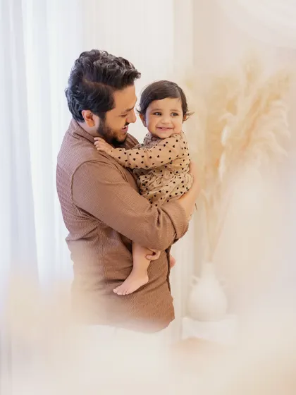 A heartwarming father-daughter portrait. The dad holds his smiling one-year-old daughter, their happy expressions and the soft, dreamy lighting creating a beautiful memory.