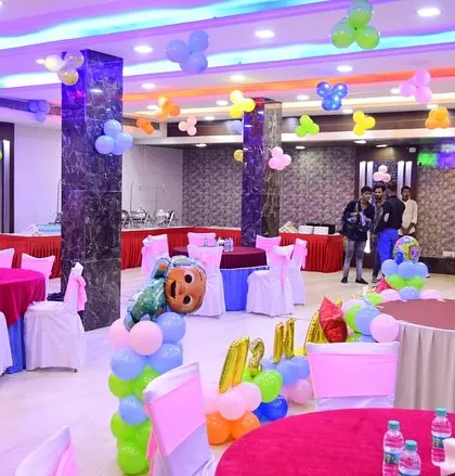 A full view of a banquet hall decorated for a birthday party. You can see the guest tables, ceiling balloons, and the main cake table area.