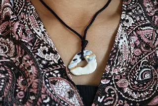 A unique, open-circle ceramic pendant with touches of gold, hanging on a black cord. It's a perfect example of modern ceramic jewelry.