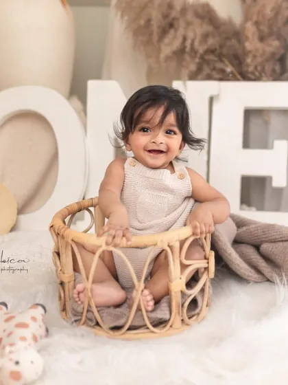 A joyful baby boy in a basket, celebrating his first year. The "ONE" sign and rustic props create a charming setup for a first birthday photoshoot.