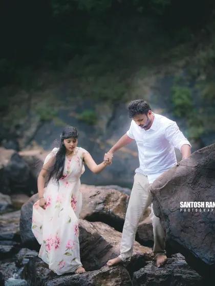 A candid moment of the groom helping his partner navigate the rocky terrain near the waterfall.