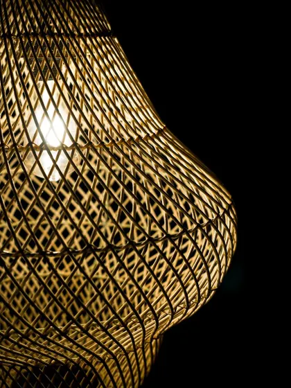 A detailed shot of the lit gourd lamp, focusing on its curved silhouette. The light accentuates the three-dimensional quality of the weave, turning the lamp into a radiant sculpture.