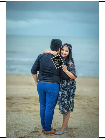 A sweet hug from behind on the beach, with the mom-to-be sharing the sonogram with the camera.