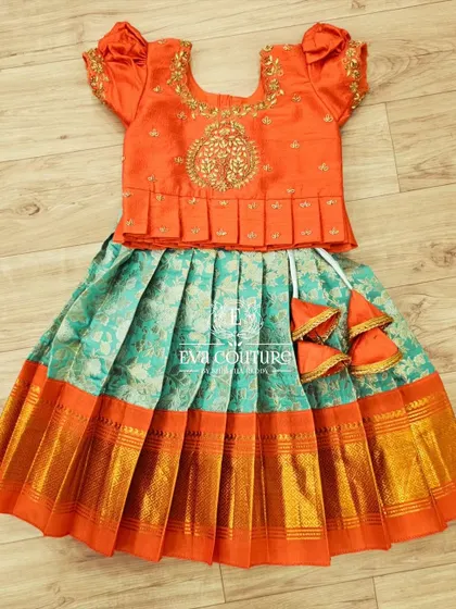A flat-lay of a beautiful orange and sea-green Banarasi lehenga. The blouse features a pleated peplum and 'tree of life' embroidery.