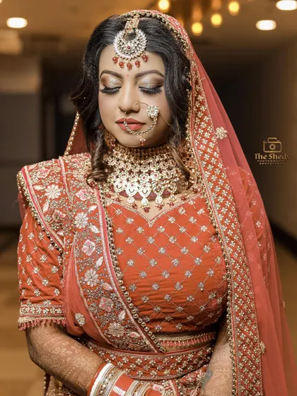 A classic, elegant portrait of a bride in a beautiful orange-red lehenga. Her serene expression and stunning jewelry are the focus of this shot.