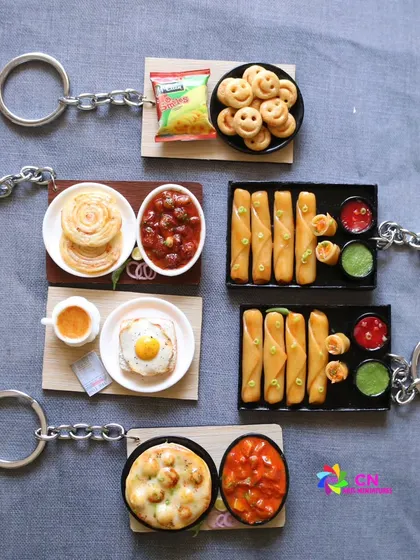 A collection of five different food keychains, including parotta with curry and spring rolls.