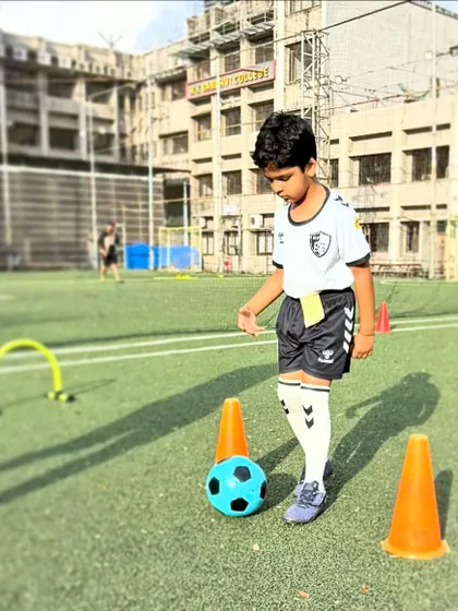 A young player pauses to assess his path through a cone and hurdle drill, learning to think strategically while maintaining ball control.