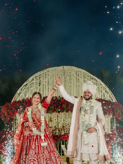 A triumphant moment for the newly married couple under a sky of fireworks and confetti. This shot captures the peak of celebration and happiness.