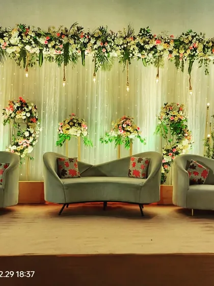 A closer look at a sophisticated reception stage. The modern grey sofas with floral cushions are set against a backdrop of white drapes, fairy lights, and beautiful pastel floral arrangements.