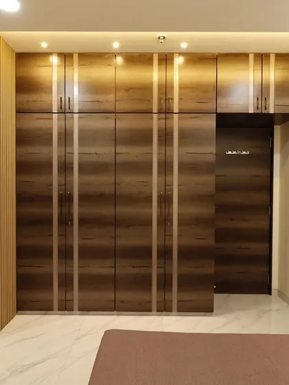 A guest bedroom in a Malad 4BHK, featuring floor-to-ceiling wardrobes in a dark wood finish with sleek vertical inlays. The room also includes a compact dressing table with a large mirror.