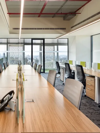 A long-shot of the workstation rows in a contemporary office. The design emphasizes clean lines and an uncluttered environment to enhance focus, with large windows providing expansive views and natural light for employees.
