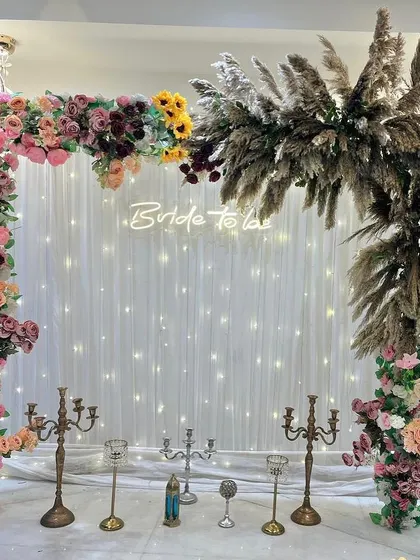 A beautiful 'Bride to be' backdrop for a bridal shower. The decor features a floral arch with pampas grass and a custom neon sign.
