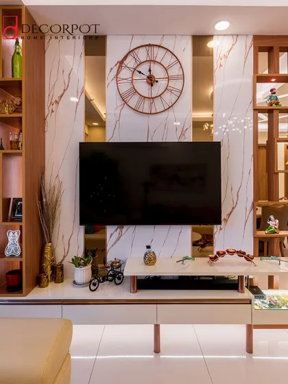 This TV unit is part of a larger display, featuring a white marble panel with rose-gold veining and a large statement clock. The open wooden shelves on either side provide ample space for decor.