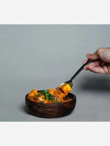 An interactive shot of the paneer masala, with a hand taking a spoonful. This helps convey the texture of the gravy and the softness of the paneer, making the dish more tempting.