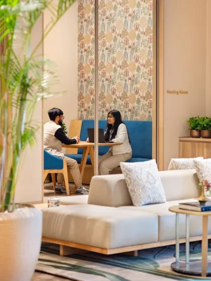 A meeting pod within the Godrej Woods Clubhouse, demonstrating the integration of work facilities into community spaces. The use of plants and patterned partitions creates a semi-private yet connected workspace.