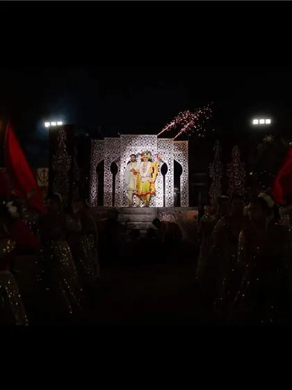 An aisle of light for the royal couple. Dancers with red flags line the path, creating a dramatic and regal walkway leading to the varmala stage.