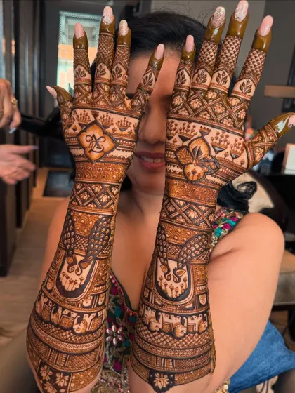 This full-coverage bridal mehndi features the couple's initials, "SK", as a central element on the back of the hands. The design is rich with traditional symbols like the hastmelap (joining of hands) and gathbandhan (tying the knot).
