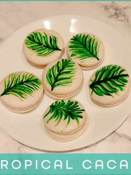 Our Tropical Cacao Macarons. These feature a rich chocolate filling and are decorated with a hand-painted tropical leaf, combining classic flavor with an artistic touch.