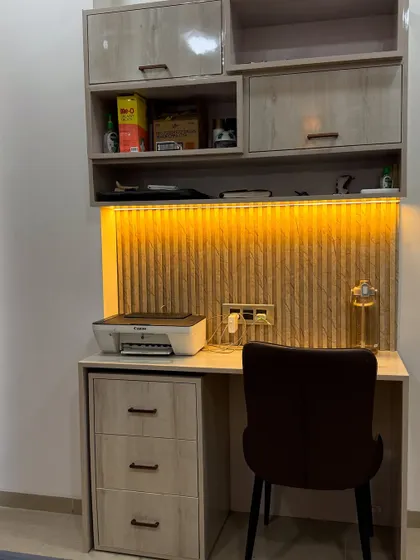 A compact study table with a fluted wooden back panel and warm LED lighting. The overhead cabinets provide ample storage for books and files.