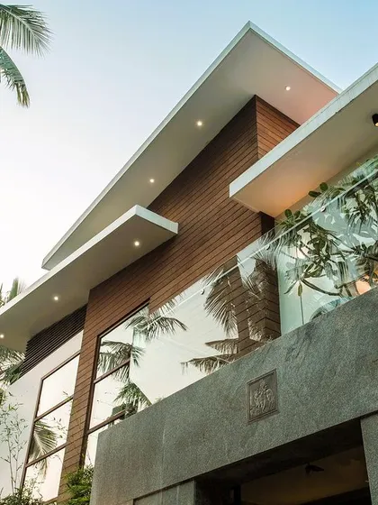 An upward view of the facade, highlighting the cantilevered rooflines, glass balcony railings, and the reflection of palm trees in the large windows.