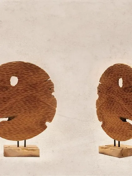 These two disc-shaped artifacts are carved with a ribbed texture and feature natural imperfections. They have an almost mask-like quality, adding a touch of mystery and character.