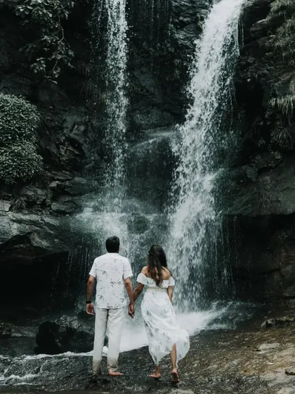The couple seen from behind, holding hands as they face a majestic waterfall, symbolizing their journey together.