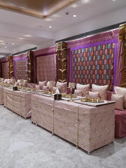 A luxurious indoor setup for a traditional event, featuring rich purple and gold fabrics, carved wooden pillars, and comfortable seating arrangements for guests to enjoy their meal.