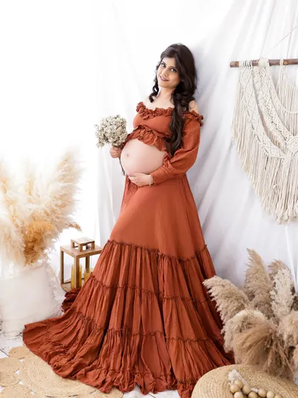 A lovely portrait in a boho-chic setting. The mom-to-be wears a beautiful rust-colored dress that complements the earthy tones of the studio.