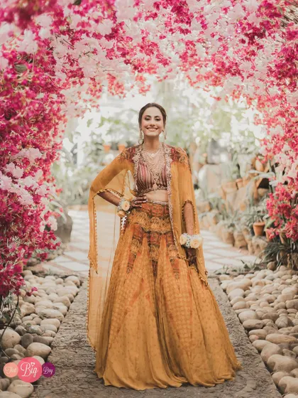 A full-length portrait of Bhavita, smiling brightly, framed by a tunnel of pink and white flowers.