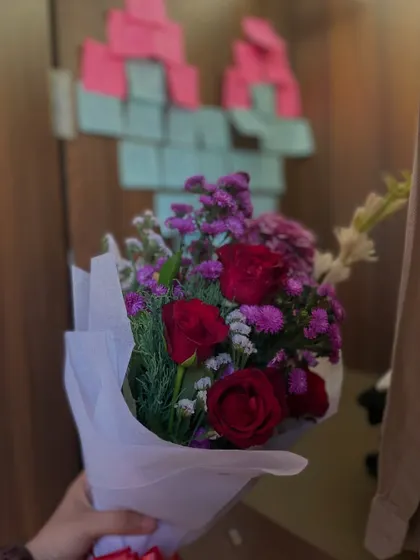 A simple, sweet, and beautiful hand-held bouquet of red roses and purple filler flowers, perfect for a spontaneous romantic gesture.