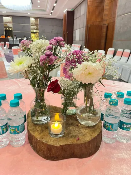 A rustic and charming centerpiece for a pastel-themed event. A collection of small glass vases with mixed flowers sits on a natural wood slice, with a small candle adding a warm glow.