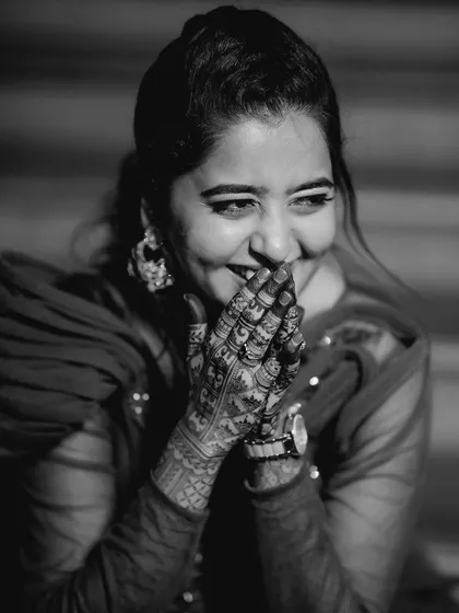 A candid black and white photo of a bride-to-be laughing, her hands with intricate henna covering her mouth. This shot captures a moment of pure, uninhibited joy.
