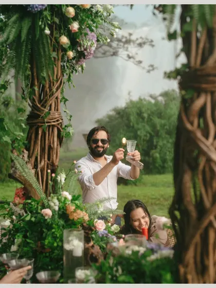 A guest raises a glass for a toast at the intimate reception table. The lush, natural decor and the waterfall in the background make this a truly memorable dining experience.
