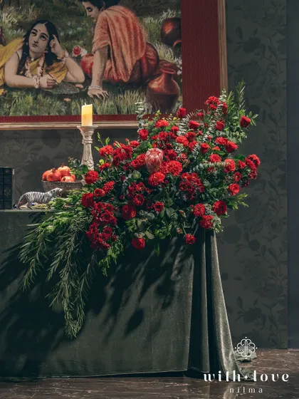 A cascading floral arrangement on a velvet-covered table. The deep reds and lush greens create a sense of opulence and drama, perfectly in tune with the artistic theme.