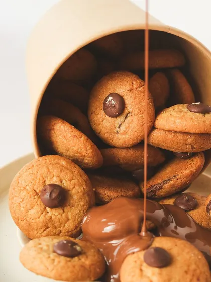Our mini chocolate chip cookies are perfect for snacking. Here they are, tumbling out of a cup with a cascade of melted chocolate.