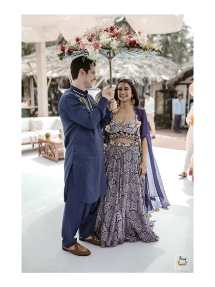 A unique shot of the groom holding a floral umbrella for the bride at their Goa Mehndi.