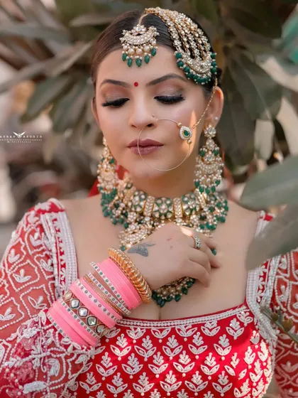 A serene close-up of the bride with her eyes closed, highlighting her flawless makeup. The contrast between the red outfit, green jewellery, and pink bangles is beautifully captured.