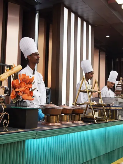 A line of our chefs in crisp white uniforms, ready for service at an elegant indoor buffet. Their poised and professional stance reflects the quality of the cuisine they are about to serve.