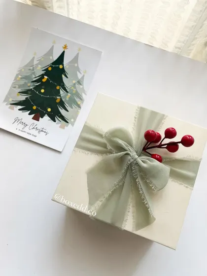 A beautifully wrapped Christmas gift box with a sage green chiffon ribbon and festive red berries.