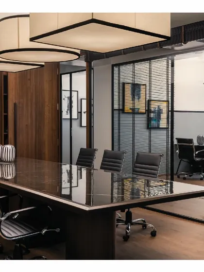 The conference room in the 'Shadows' project, seen through glass partitions. The dark furniture and grey walls create a formal and modern look, while the large, custom-designed overhead lights add a sculptural element.